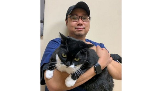 North Shore Animal Hospital  Michael - Lead Technician holds a large black and white cat in their arms, standing indoors against a beige wall.