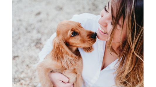 A person smiling while holding a golden retriever puppy, both looking at each other lovingly.