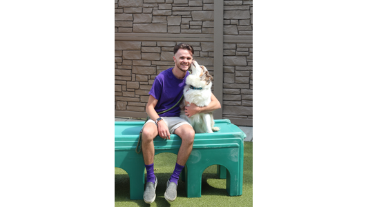 Andrew -Animal Care Attendant (ACA) getting an affectionate lick on the cheek from a fluffy white and merle dog.