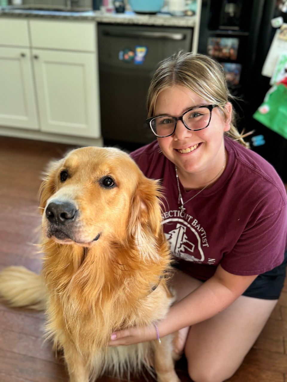Ava -Animal Care Attendant beside a golden retriever in a kitchen setting.