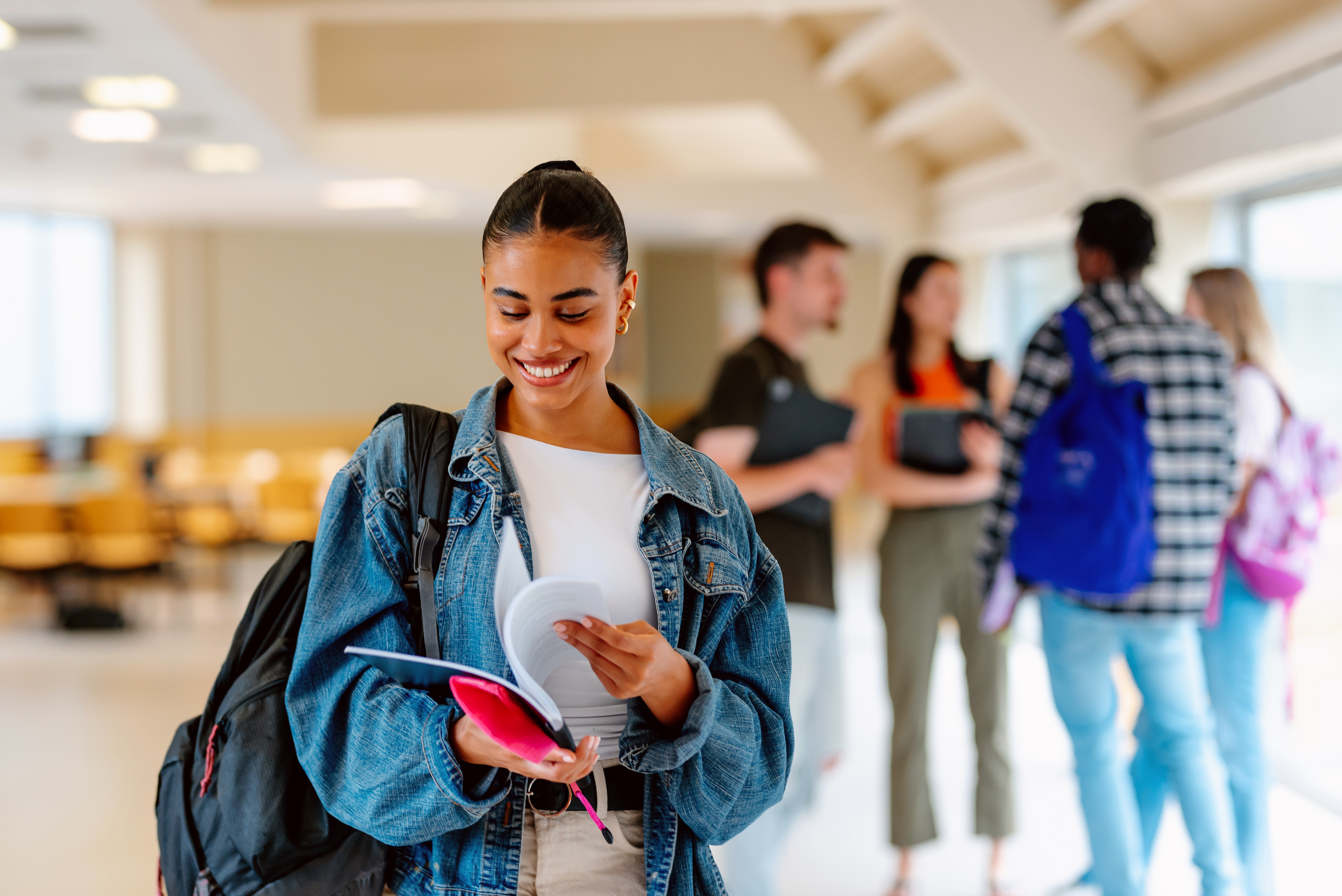 Smiling student carrying a backpack and notebook in a school hallway
