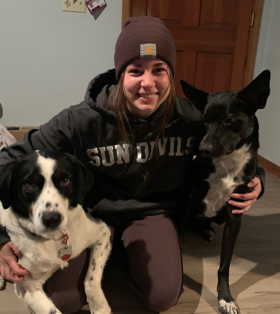Maddy -Pet Care Team Leader kneeling indoors while smiling and posing with two black and white dogs