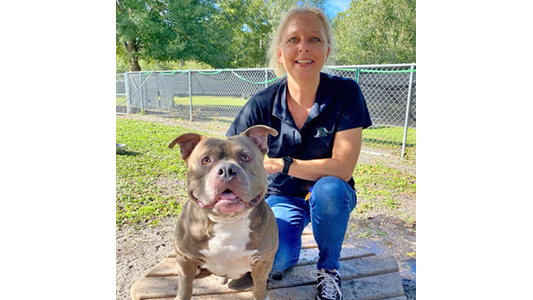 Bass Pet Resort General Manager Darlene Bass smiling outdoors with a gray and white pitbull.