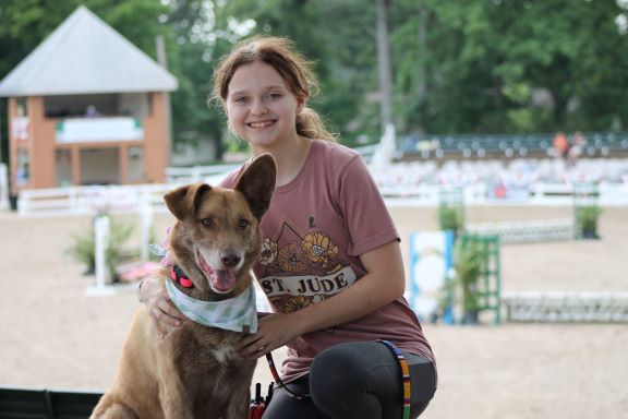 Savannah -Lead Animal Care Attendant with a happy brindle Shepherd mix wearing a bandana at an outdoor community event